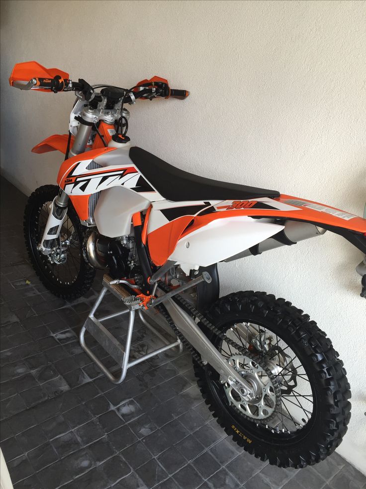 an orange and white dirt bike parked next to a wall