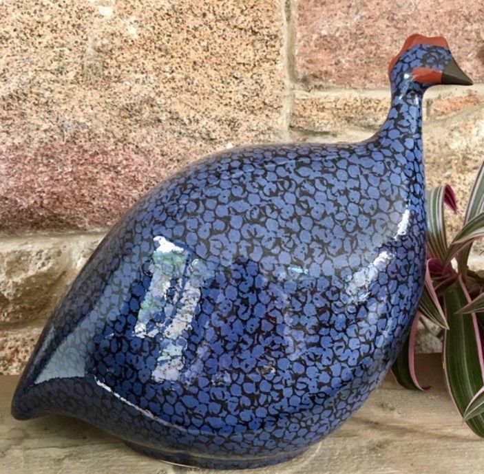 a blue ceramic bird sitting next to a potted plant on a stone wall background