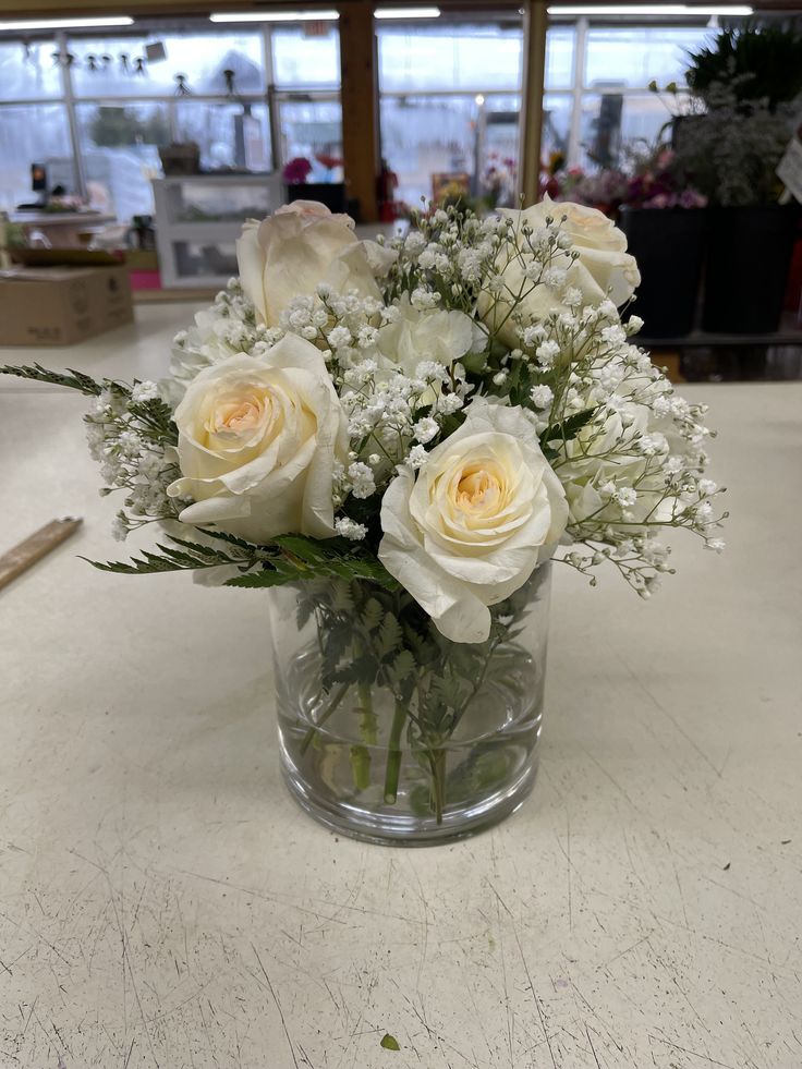 white roses and baby's breath in a clear vase on a countertop at a store