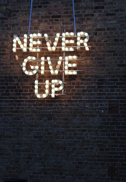 a sign that says never give up on the side of a brick wall with neon lights