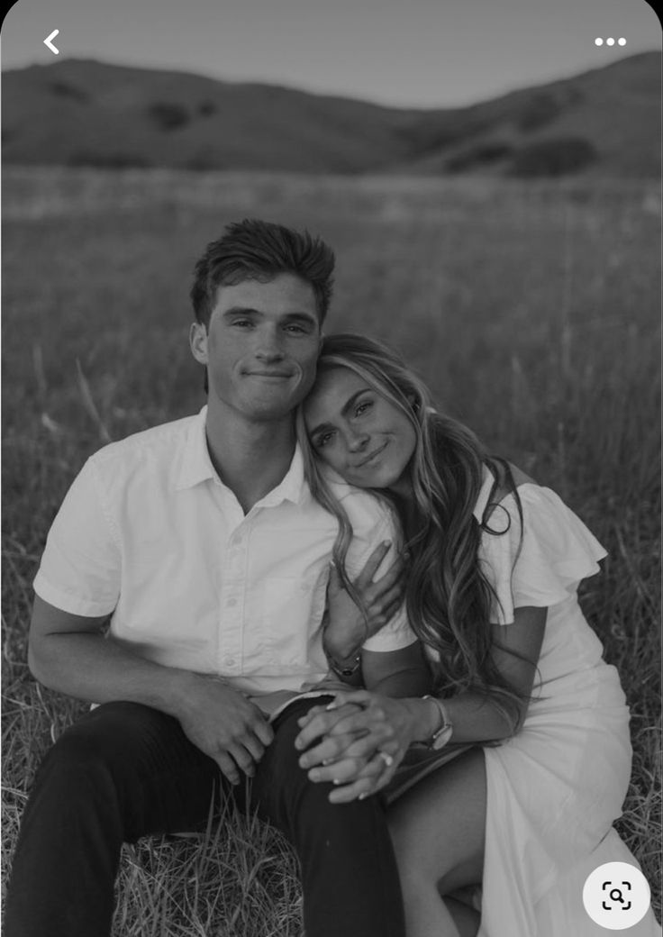 a man and woman are sitting in the grass with their arms around each other, looking at the camera