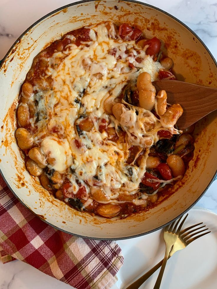 a skillet filled with pasta and sauce on top of a table next to a fork