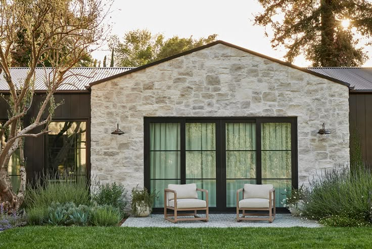 two chairs sitting in front of a stone building with glass doors and windows on each side