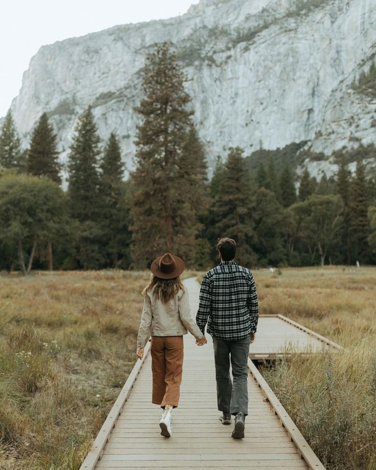 a man and woman walking down a wooden walkway in front of a large mountain range