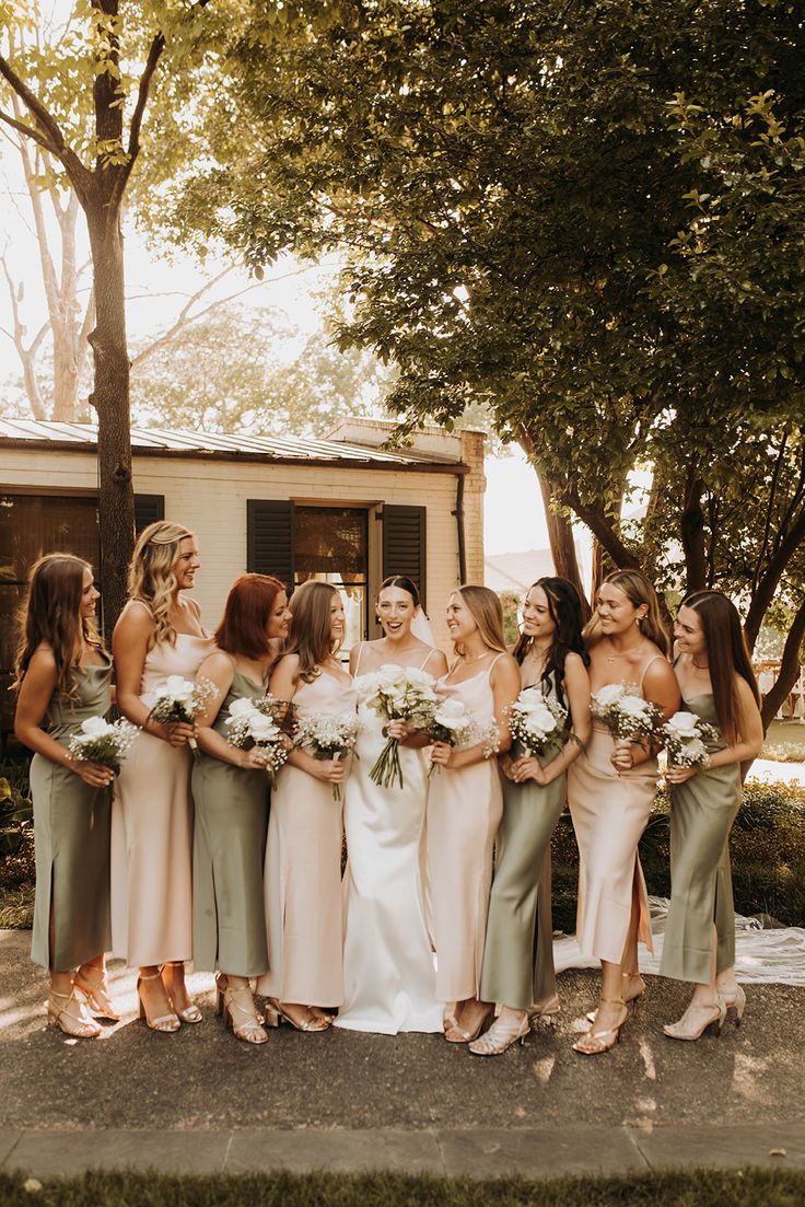 a group of women standing next to each other in front of a house holding bouquets