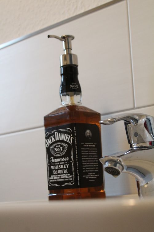 a bottle of jack daniels whiskey sitting on top of a sink next to a faucet