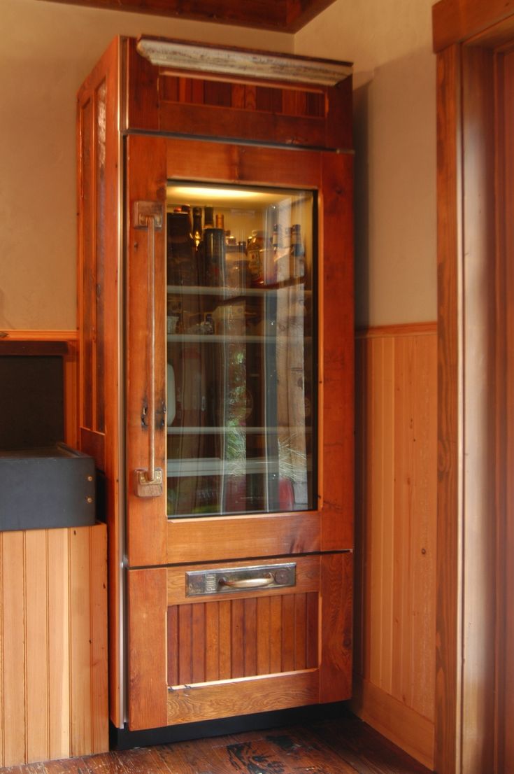 a wooden cabinet with glass doors in a room that has wood paneling on the walls