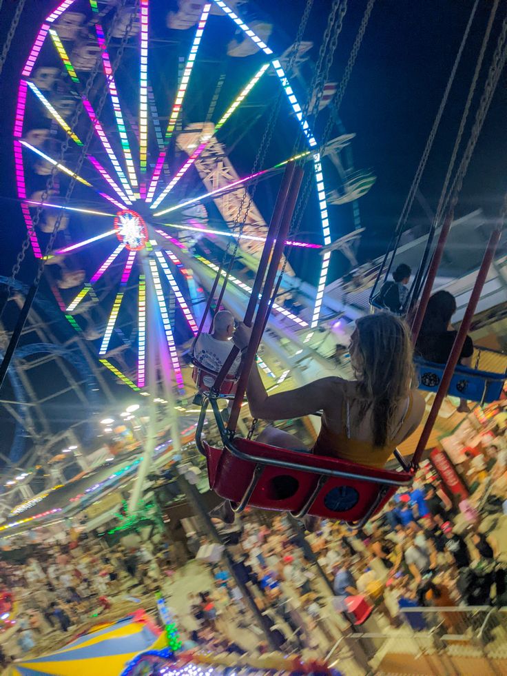 a woman is riding on a swing at an amusement park with ferris wheel in the background