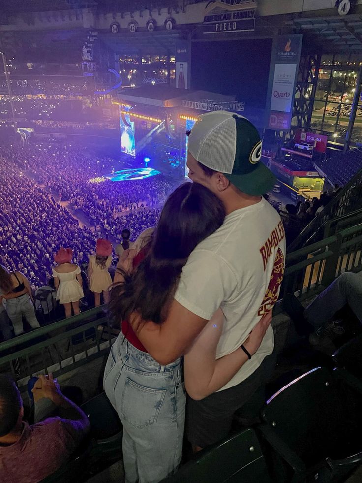 a man and woman embracing in front of an arena full of people at a concert