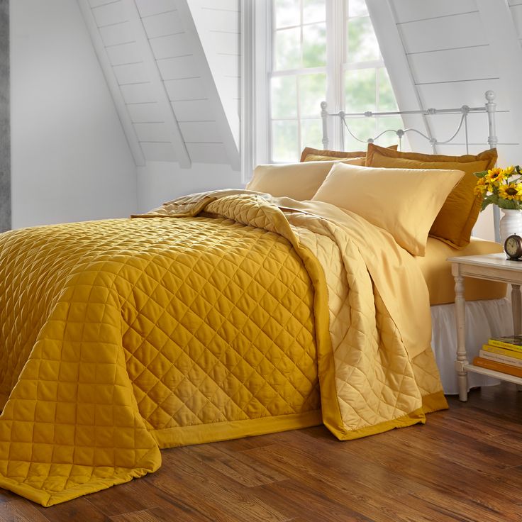 a bed with yellow comforter and pillows in a room next to a window,