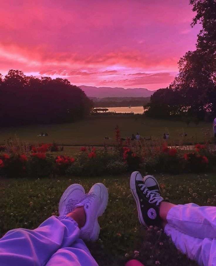 two people sitting in the grass with their feet up against each other as the sun sets