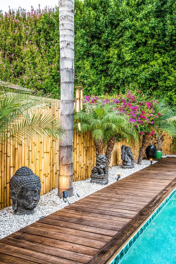 a wooden walkway next to a swimming pool surrounded by trees and plants with buddha statues on each side