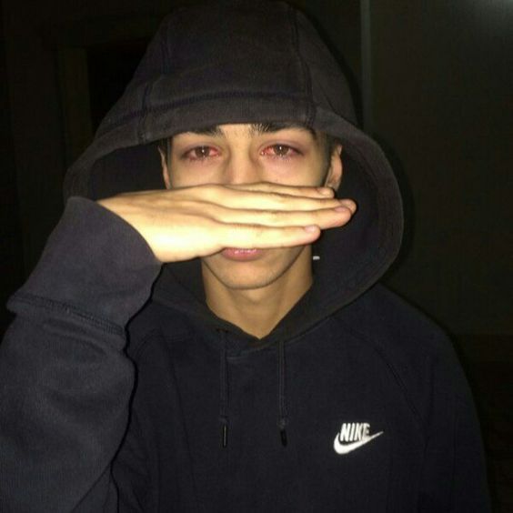 a young man covers his face with his hands as he poses for the camera in front of him