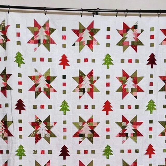 a white quilt with red and green christmas trees hanging from it's side on a clothesline