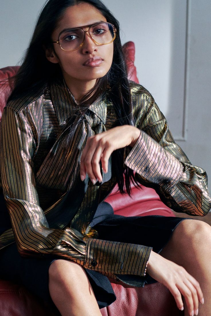 a woman sitting on top of a red couch wearing glasses and a metallic shirt dress