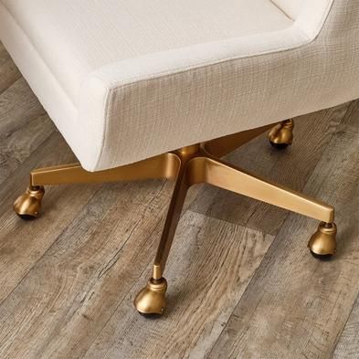 an office chair with gold casteors sits on a wood floor