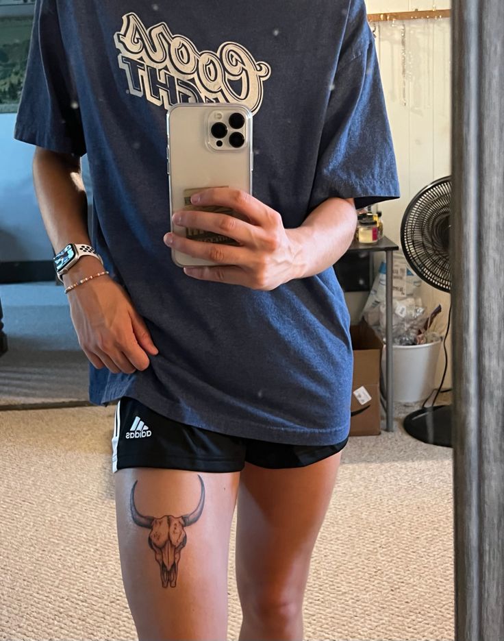 a person with tattoos on their legs holding a cell phone and taking a selfie