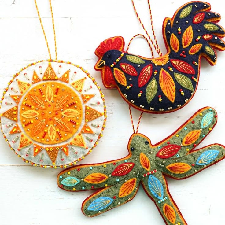 three handmade ornaments hanging from strings on a white surface with an orange and blue bird