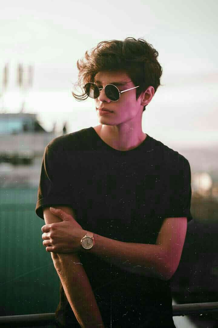 a young man wearing sunglasses standing on top of a roof with his arms crossed and looking off into the distance