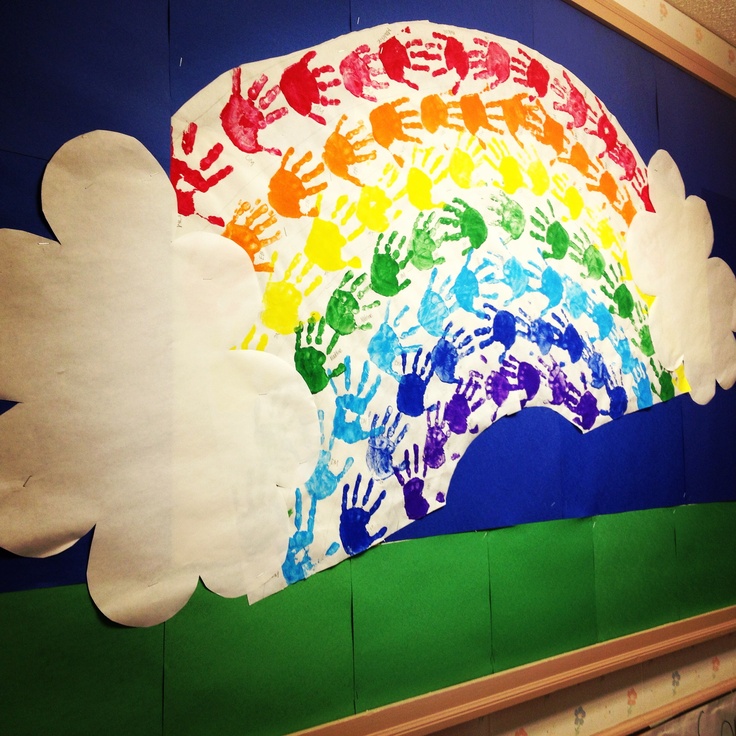 a bulletin board with rainbows and handprints on the front, hanging in a classroom