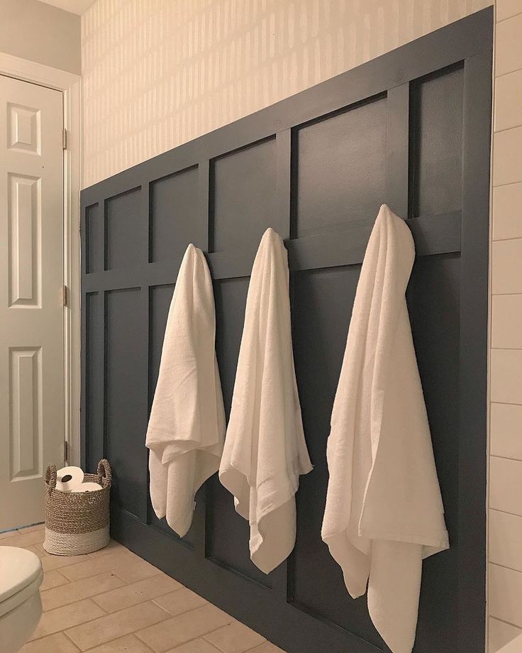 three white towels hanging on the side of a black paneled wall in a bathroom