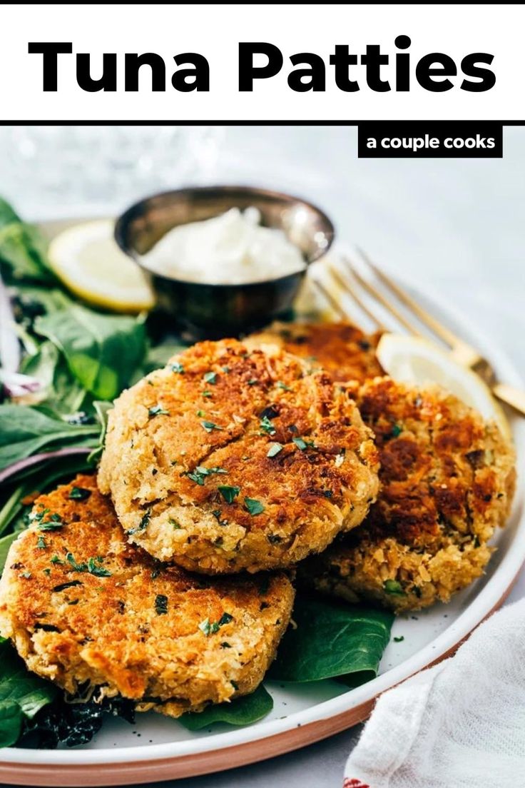 two crab cakes on a plate with spinach and lemon wedges next to it