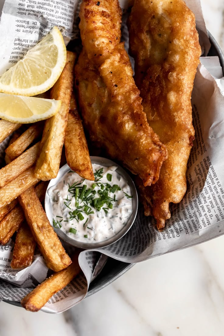 fried fish and fries are served with sour cream sauce on the side, along with lemon wedges