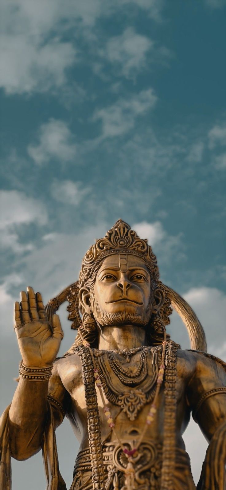 the statue is holding his hands up in front of blue sky with clouds behind it