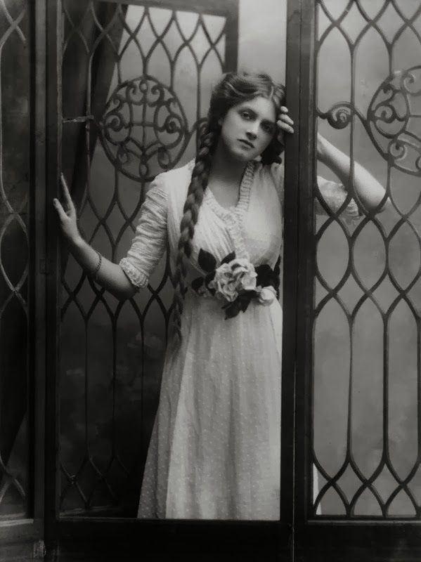 an old photo of a woman standing in front of a gate with her hands on her head