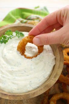 a person dipping dip into a wooden bowl filled with onion rings and sour kraut