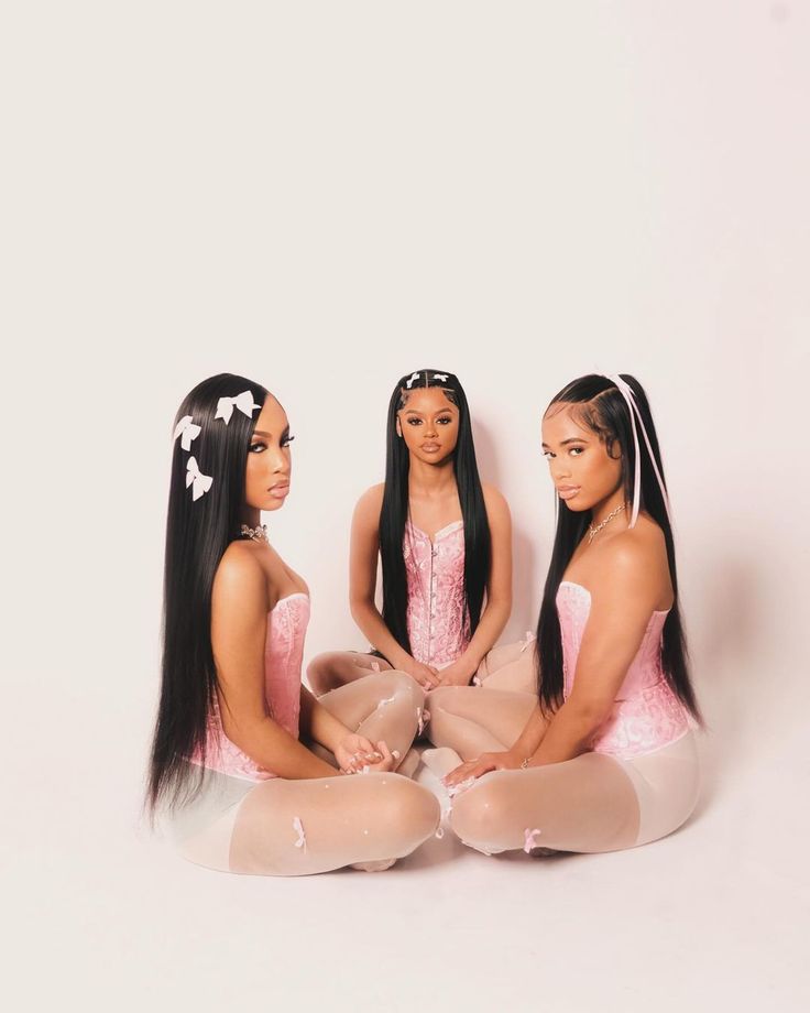 three beautiful women sitting on the ground in front of a white wall with long hair