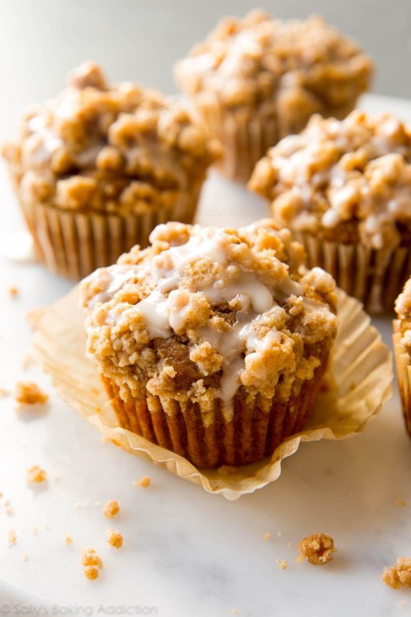 several muffins with icing and crumbs sitting on a white surface