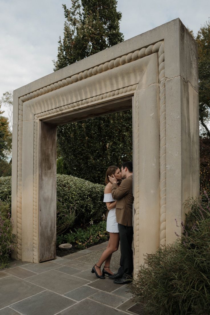 a man and woman standing in front of a stone arch