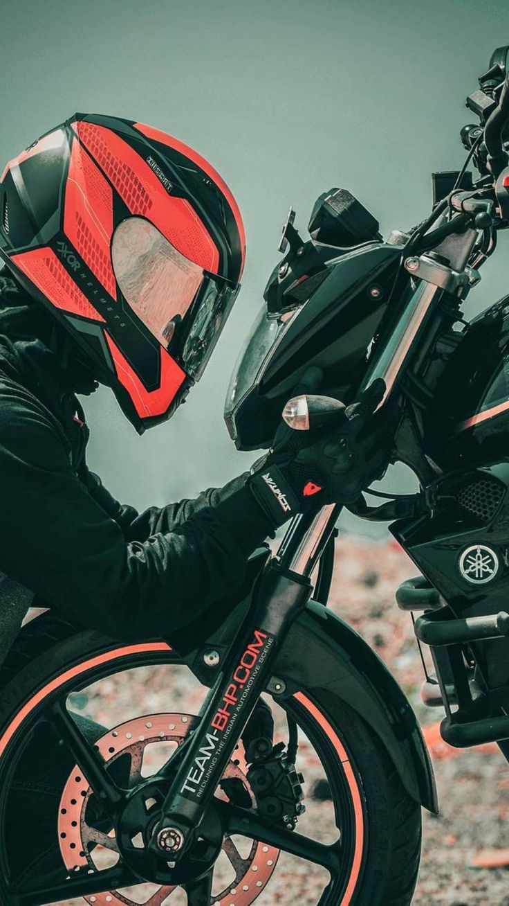 a man wearing a red helmet and black jacket sitting on a motorcycle with orange rims