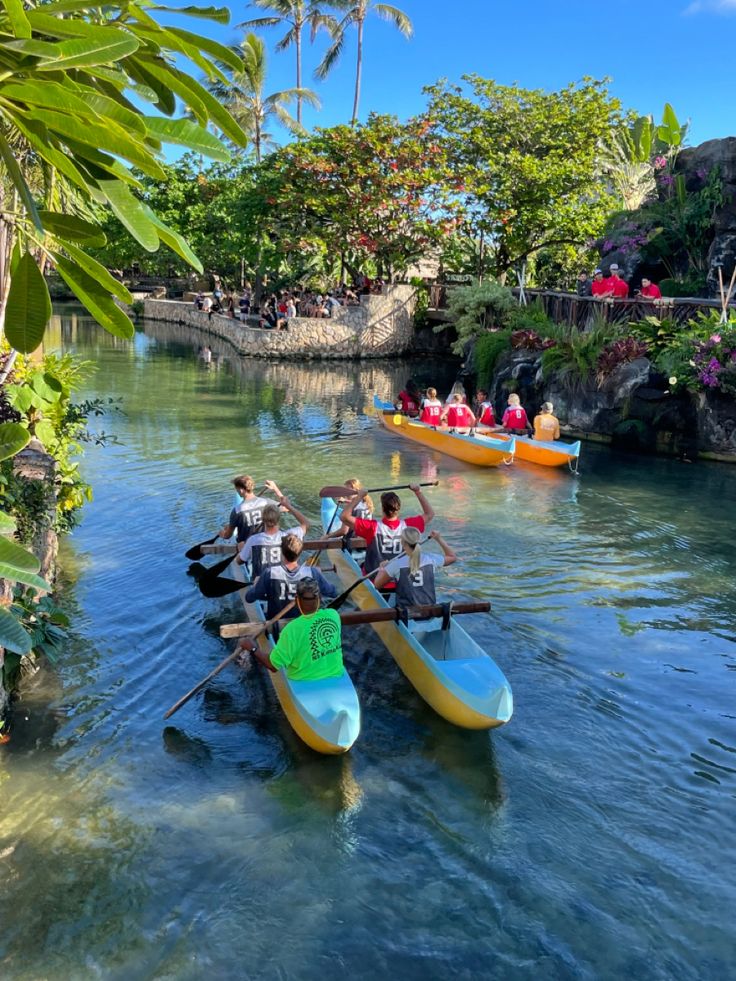 several people in canoes paddling down a river surrounded by greenery and trees