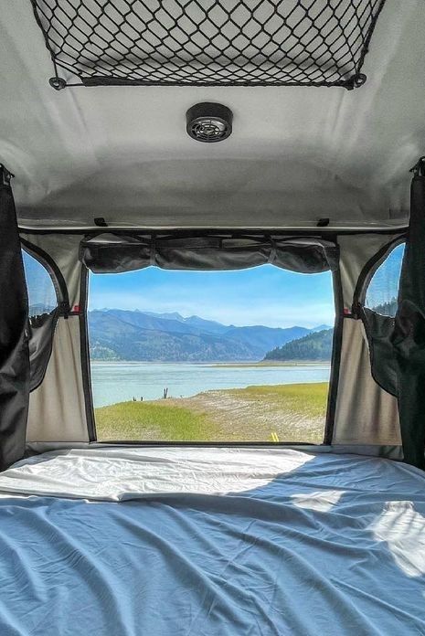 the view from inside an rv looking out at water and mountains in the distance, with a bed set up between two windows