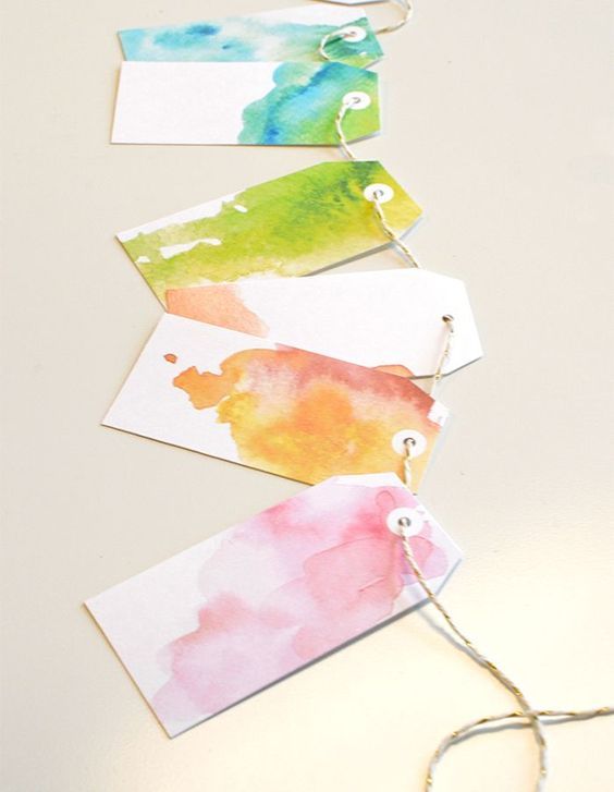 four watercolor tags hanging from string on white surface with twine and thread attached to them