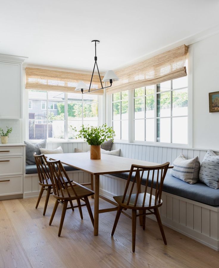 a kitchen table with four chairs and a bench in front of the window that is open