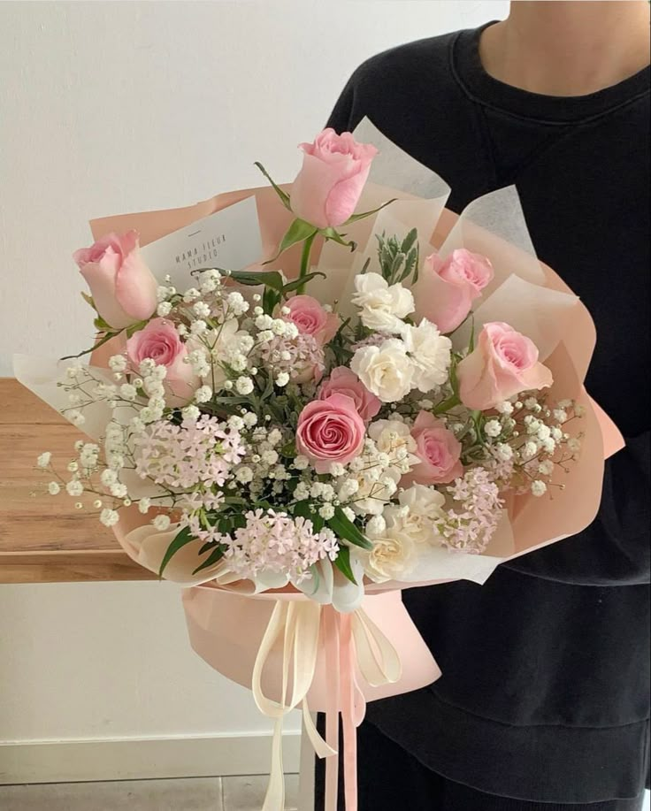 a woman holding a bouquet of pink roses and white carnations in her hands