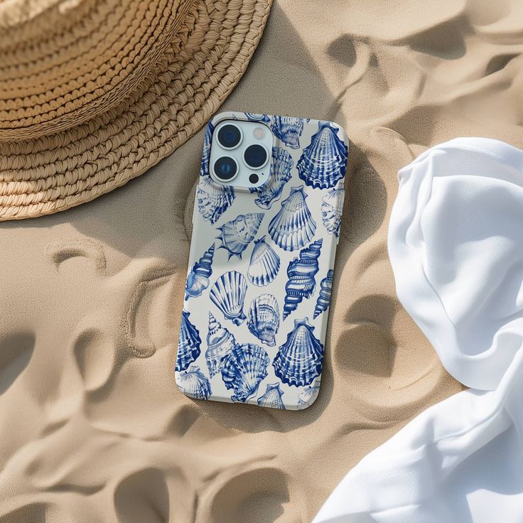 an iphone case sitting on top of a beach next to a straw hat and white towel