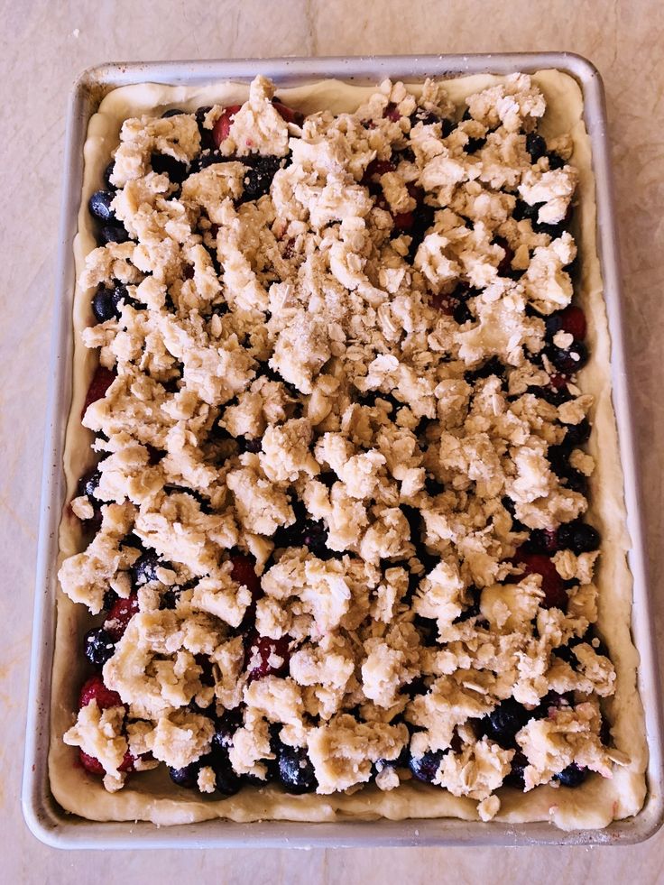 an uncooked blueberry crumbled dessert in a pan on a table