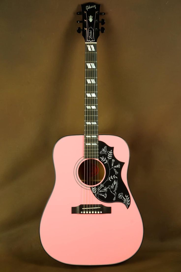 a pink acoustic guitar sitting on top of a brown background