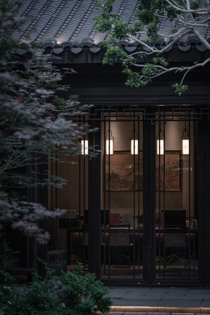 an entrance to a building with glass doors and trees in the foreground at night