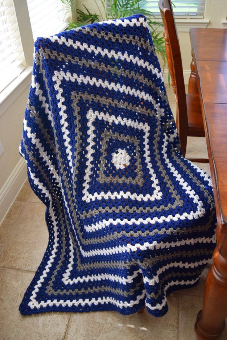 a blue and white crocheted blanket sitting on top of a wooden table next to a chair