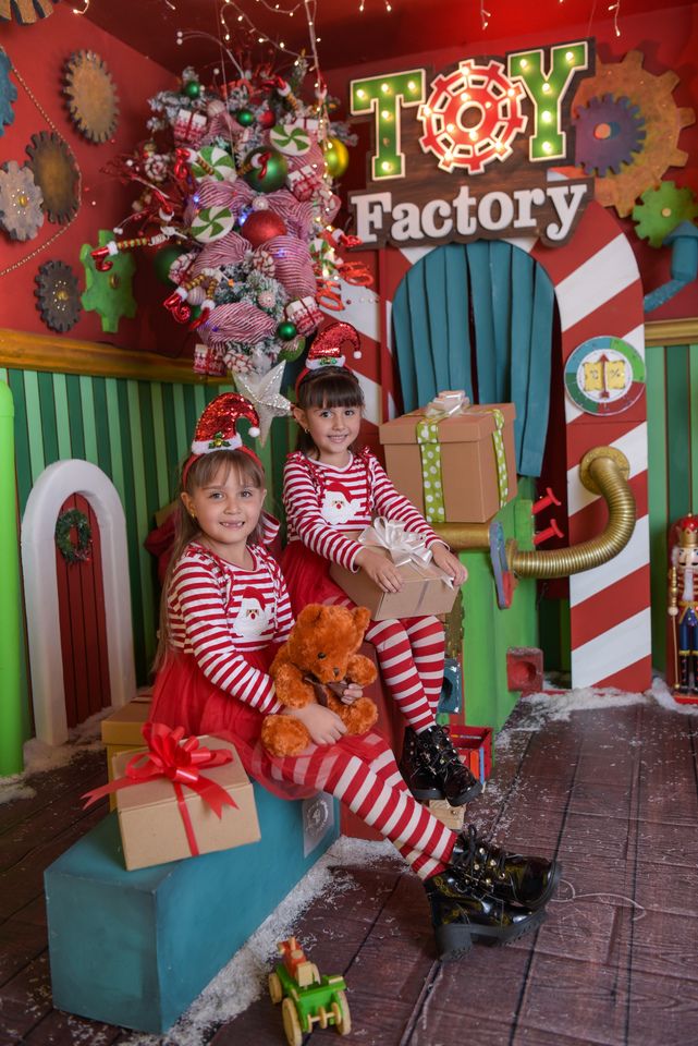 two children dressed in elf costumes sitting on a bench with presents and toys around them