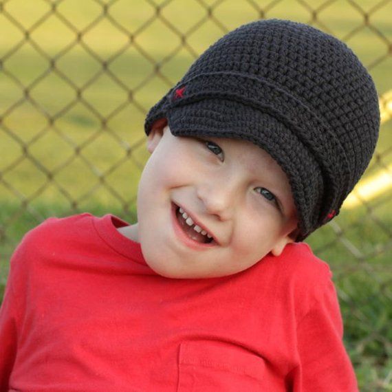 a young boy in a red shirt and black hat smiles while sitting on the grass