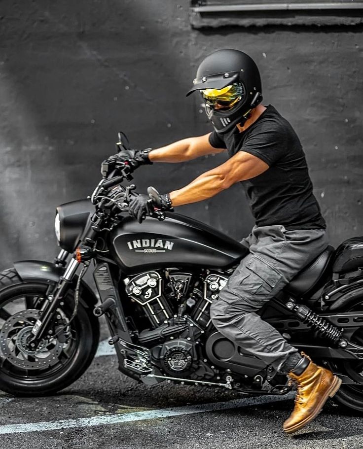 a man riding on the back of a motorcycle in front of a black wall and wearing a helmet