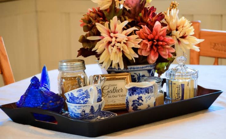 there is a tray that has some flowers in it on top of a table with blue and white dishes