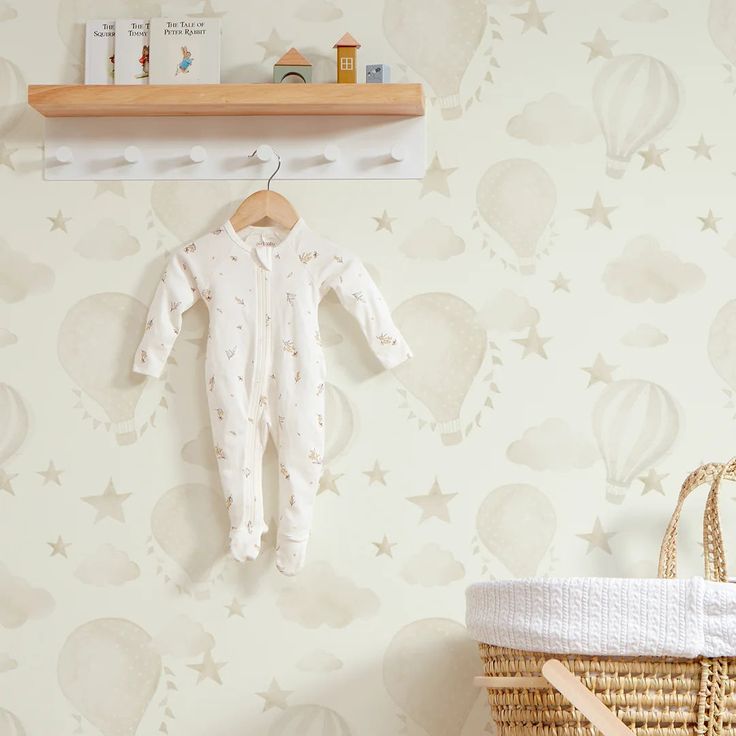 a baby's white sleepsuit hanging on a wall next to a basket and shelf