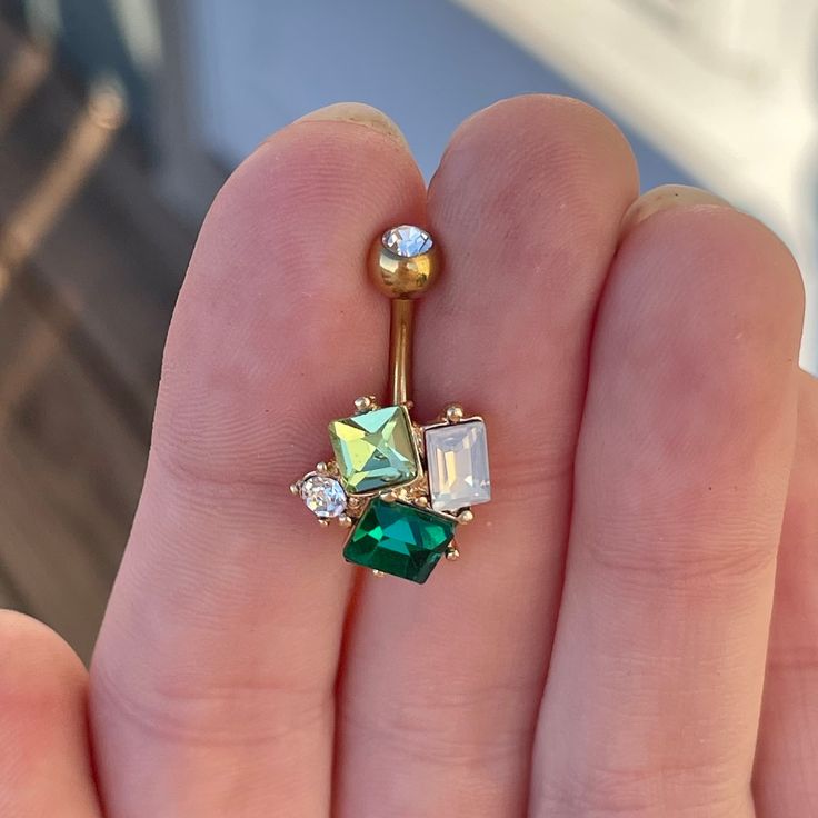 a person holding a green and white jeweled navel ring